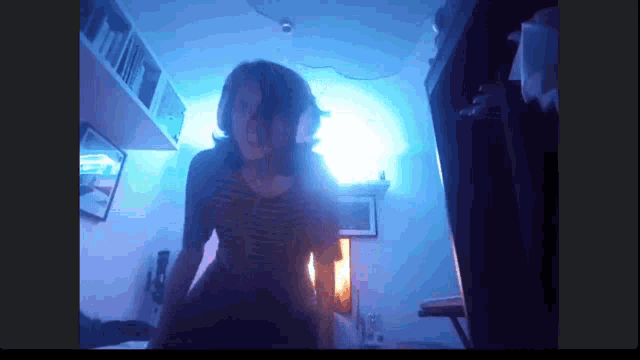 a woman in a striped shirt is dancing in a room with blue lights
