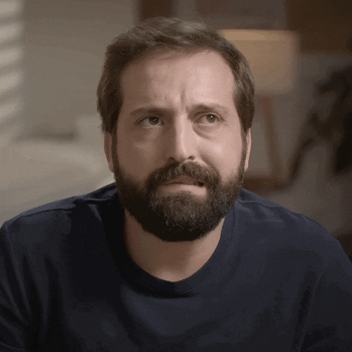 a man with a beard is wearing a blue shirt and making a funny face