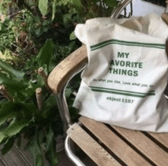 a white tote bag is sitting on a wooden chair next to a plant .