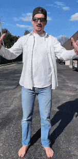 a man in a white shirt and blue jeans is standing barefoot on the street