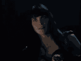 a woman with long black hair and bangs is smiling in the dark .