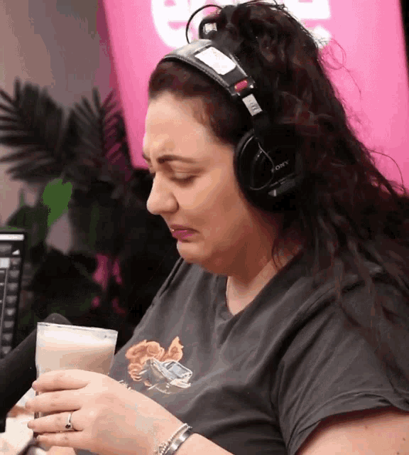 a woman wearing sony headphones is holding a cup of milk