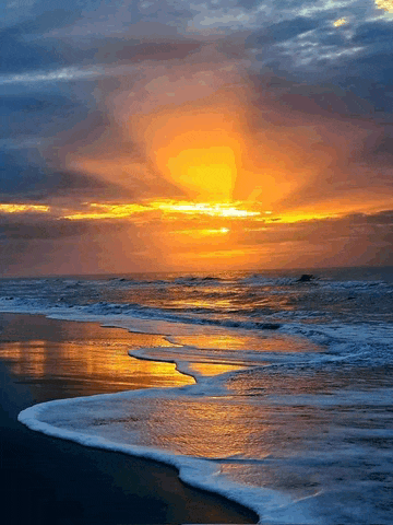 a sunset over a beach with waves crashing on the shore