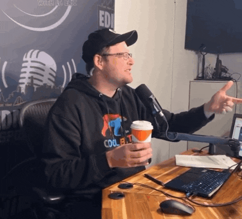 a man wearing a sweatshirt that says cool flat is sitting at a desk