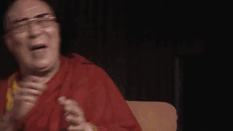 a bald man wearing glasses and a red robe is sitting on a couch and laughing .