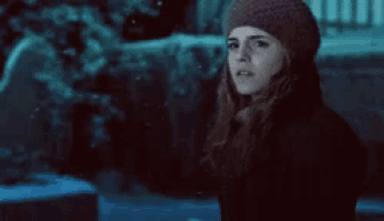 a woman wearing a knitted hat and scarf is standing in the dark looking at the camera .