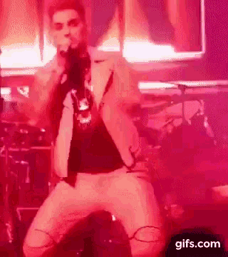 a man is singing into a microphone on a stage in front of a red background .