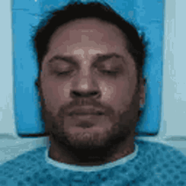 a man is laying in a hospital bed with his eyes closed and a beard .