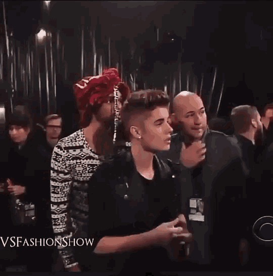 a man in a red hat is standing in a crowd with the words vsfashionshow on the bottom right