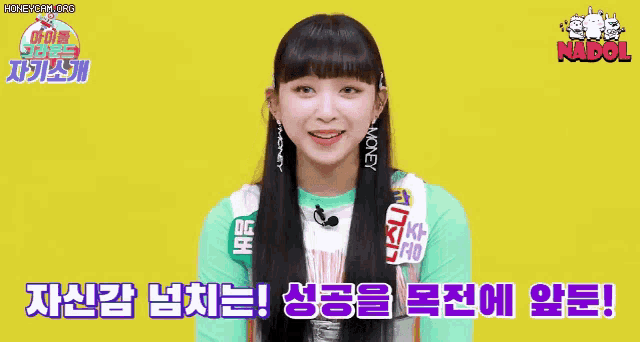 a young girl with long black hair is smiling and wearing a green shirt and earrings .