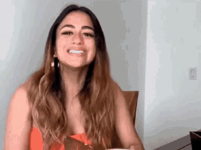 a woman is smiling while sitting at a table in front of a white wall .