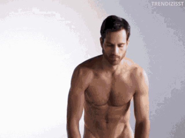 a shirtless man is standing in front of a white background and looking down .