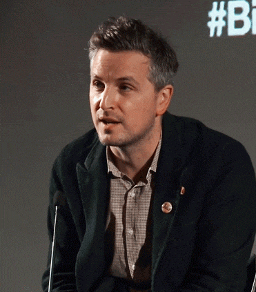 a man in a black jacket stands in front of a screen that says # bi