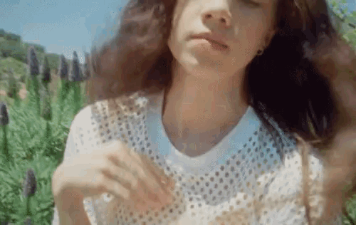 a woman in a white shirt is standing in front of a field of purple flowers
