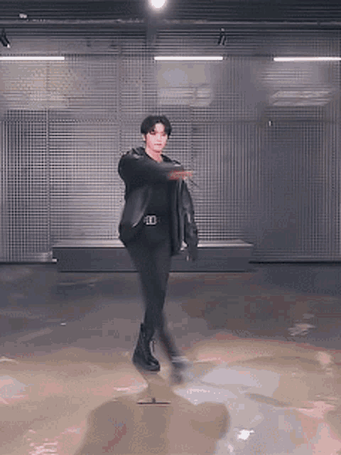 a man in a black jacket and black pants is dancing in a garage .