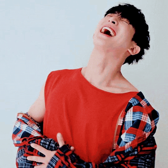 a man in a red shirt and plaid jacket is laughing with his mouth open