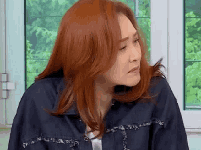 a woman with red hair is sitting in front of a window making a funny face .