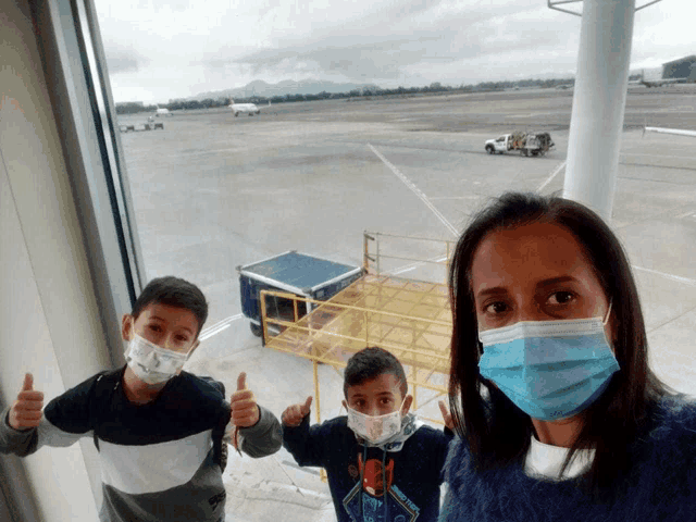 a woman and two children wearing face masks giving thumbs up