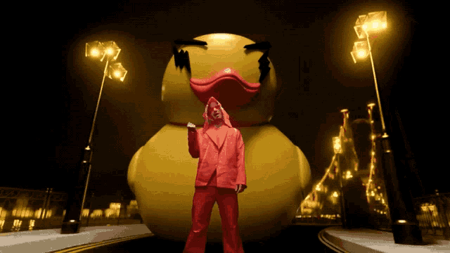 a man in a red suit stands in front of a giant yellow rubber duck