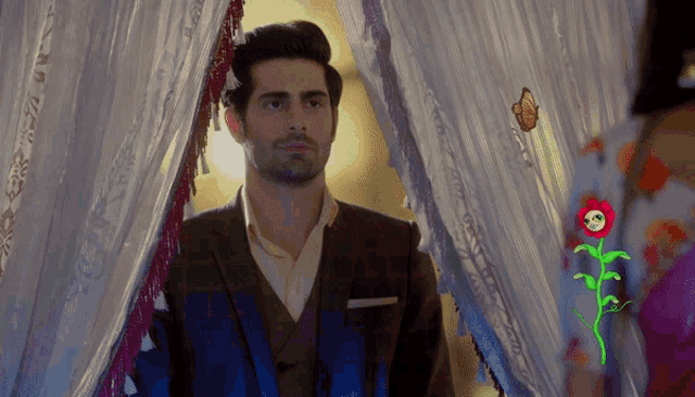 a man in a suit stands in front of a white curtain with a flower on it