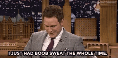 a man in a suit and tie is talking into a microphone and saying `` i just had boob sweat the whole time '' .