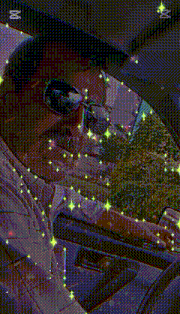 a man wearing sunglasses is driving a car with a reflection of trees in the windshield