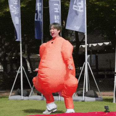 a man in an orange inflatable chicken costume is dancing on a field .