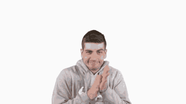 a man wearing a grey hoodie is clapping his hands together