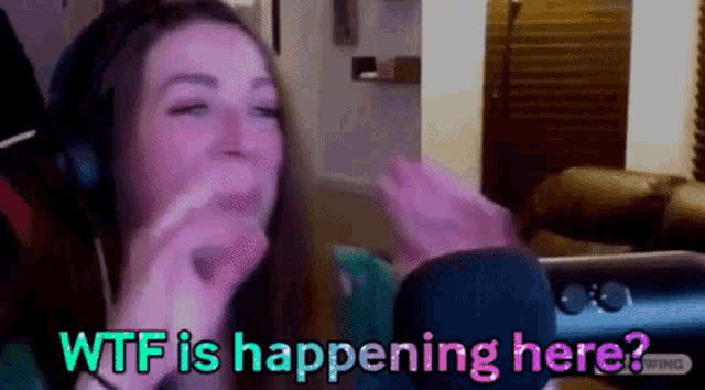 a woman wearing headphones says wtf is happening here while sitting in front of a microphone