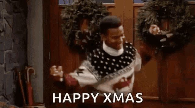 a man in a sweater is dancing in front of a door with a christmas wreath .