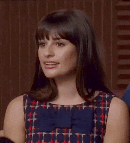 a woman in a plaid dress with a blue bow on the front is making a face .