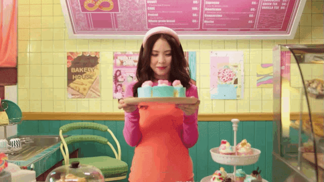 a woman holding a tray with a cake in front of a sign that says bakery house