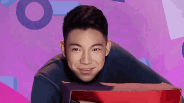 a young man is holding a red box in front of a pink background .