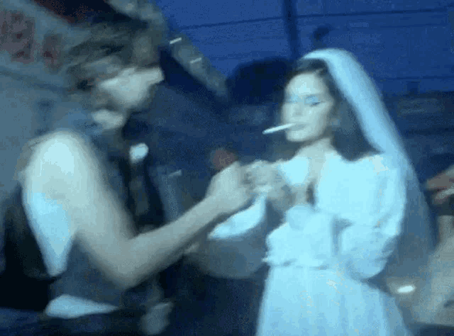 a woman in a wedding dress is smoking a cigarette next to a man .
