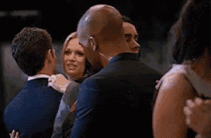 a group of people are standing around a man and a woman hugging each other .