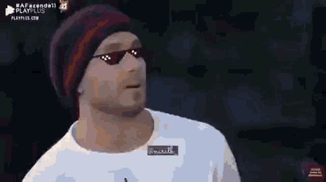 a man wearing sunglasses and a beanie is standing in front of a dark background .