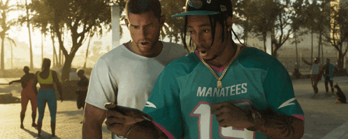 a man wearing a manatees jersey is looking at a cell phone