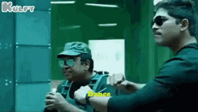 two men are standing next to each other in a room and one of them is wearing sunglasses and a hat .