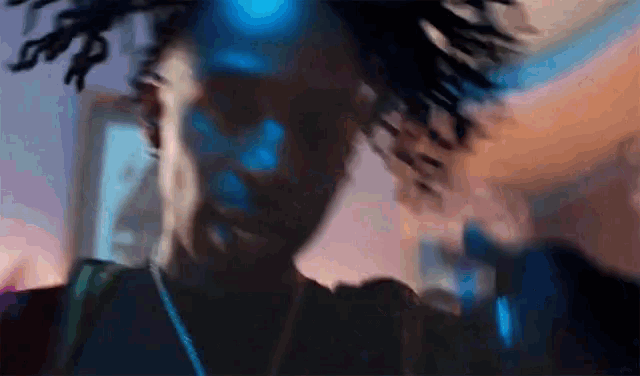 a blurry picture of a man with dreadlocks and a blue light behind him