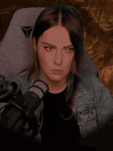 a woman in a denim jacket is making a funny face while sitting in front of a microphone