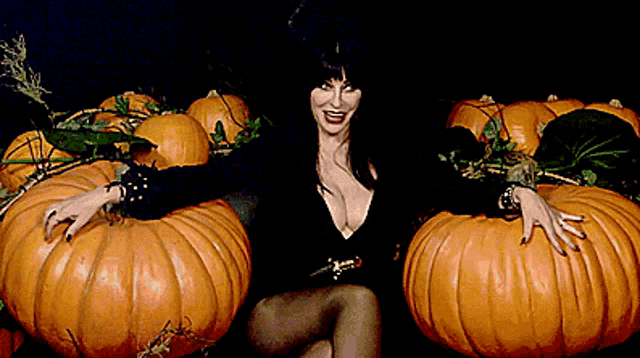 a woman in a black dress is sitting between two pumpkins