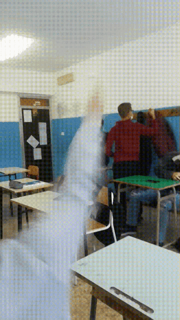 a man in a red shirt is standing in a classroom with other people
