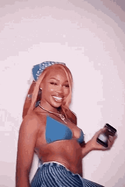 a woman in a blue bikini top and striped shorts is holding a cell phone .
