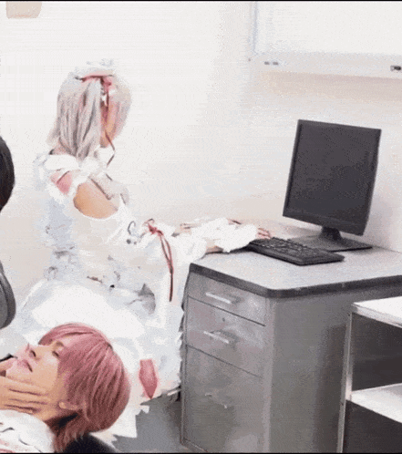 a woman in a white dress sits on a desk next to a computer monitor