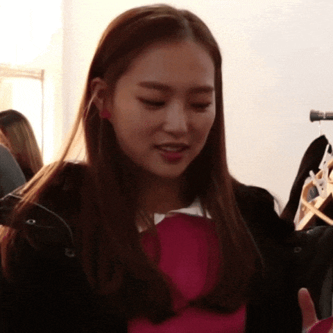 a woman wearing a black jacket and a pink shirt is standing in front of a rack of clothes