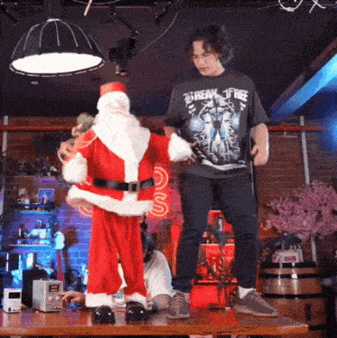 a man wearing a metallica shirt stands next to a dancing santa