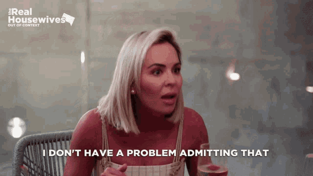 a woman sitting at a table with a glass of wine says i don 't have a problem admitting that