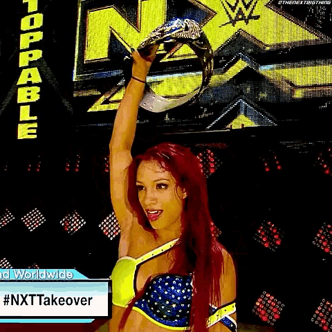 a woman with red hair is holding a trophy in front of a screen that says nxt takeover .
