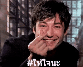 a man is smiling and making a heart shape with his fingers on his nose .