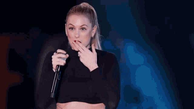 a woman in a crop top is holding a microphone and singing into it .